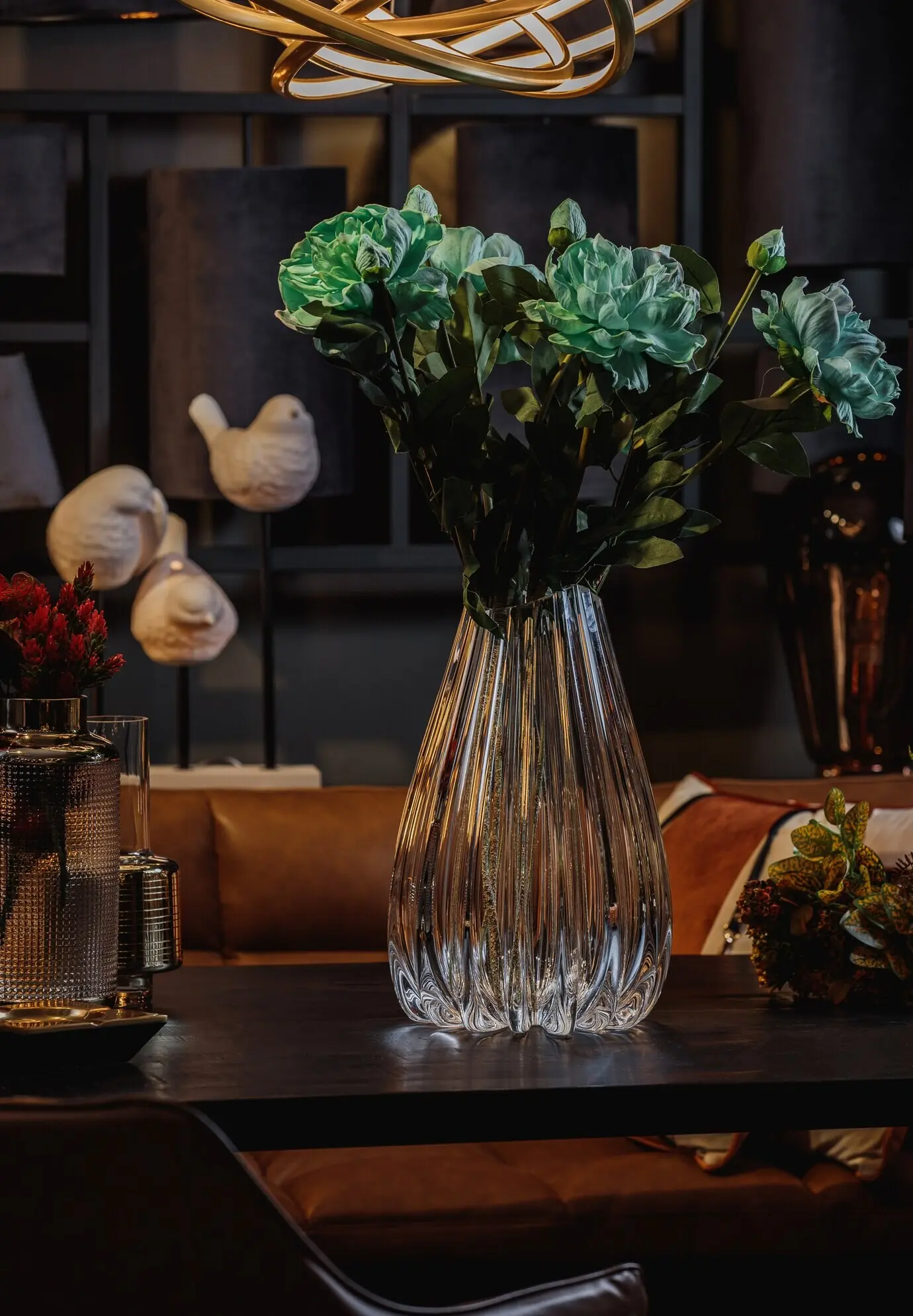 Seitenansicht einer modernen, geprägten Glasvase mit grünen Blumen auf einem Holztisch.